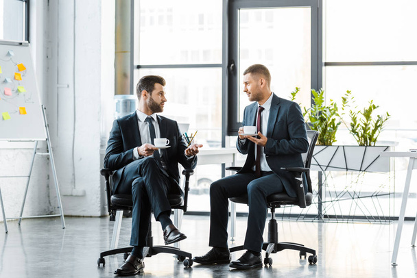 handsome businessmen talking while holding cups with drinks - Photo, image