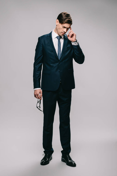 handsome businessman standing in suit and holding head on grey background  - Fotografie, Obrázek
