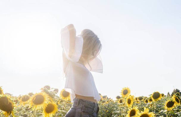 Beautiful young Caucasian woman posing in sunflower fields on sunny summer day. - Фото, зображення