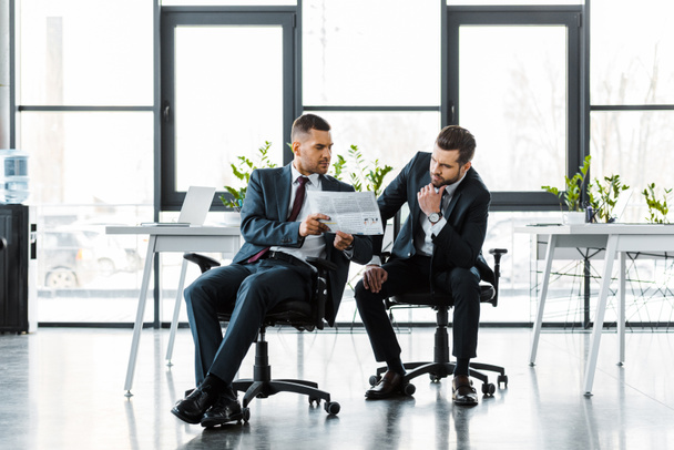 gutaussehende Geschäftsleute lesen Wirtschaftszeitung, während sie im modernen Büro sitzen  - Foto, Bild