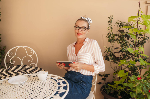 Όμορφη γυναίκα Καυκάσιος, χρησιμοποιώντας ένα tablet, ενώ κάθεται σε μια υπαίθρια καφετέρια. - Φωτογραφία, εικόνα