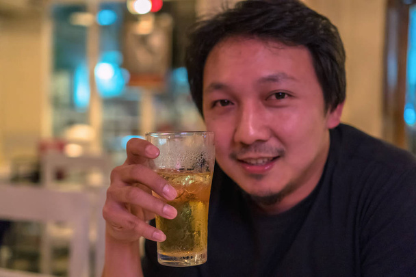 Aasialainen nuori mies onnellisuudessa toiminta ja oluen juominen pubissa ja ravintolassa, jossa on heikko valaistus, rentoutua ja juoda konsepti
 - Valokuva, kuva
