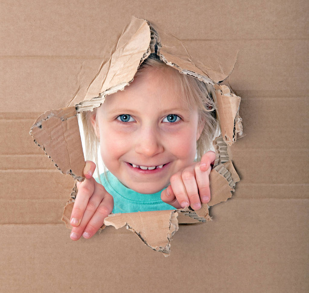 girl looking through hole in cardboard - Zdjęcie, obraz