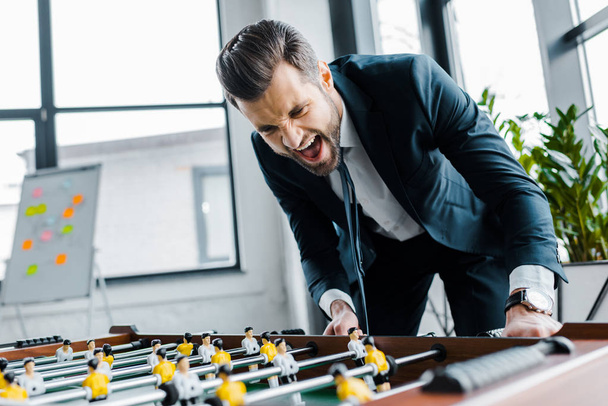 cheerful bearded businessman in formal wear playing table football  - Photo, Image