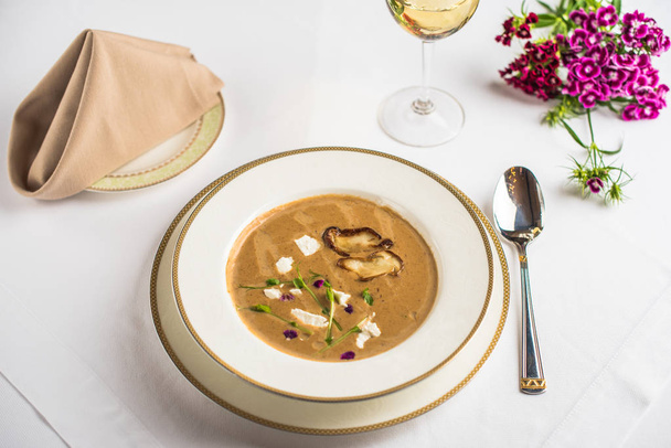 delicious cream soup with mushrooms, flowers and glass of wine on restaurant table  - Foto, Bild