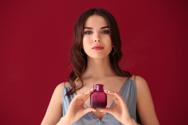 Beautiful young woman with bottle of perfume on color background - Photo, Image