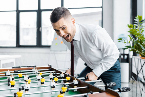 excited businessman in formal wear screaming while  playing table football  - Photo, Image
