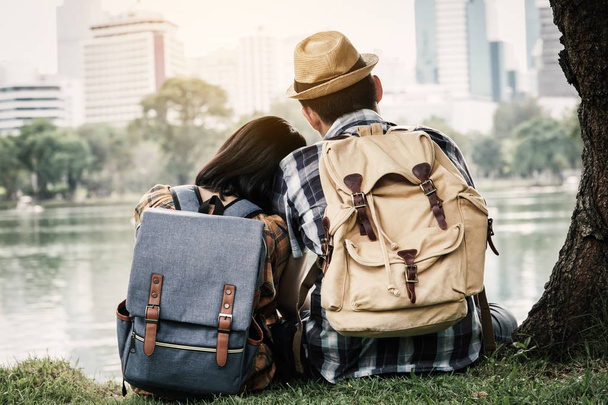 Hipster couple backpacking sitting under the tree on park background, journey on holiday concept . - Photo, image