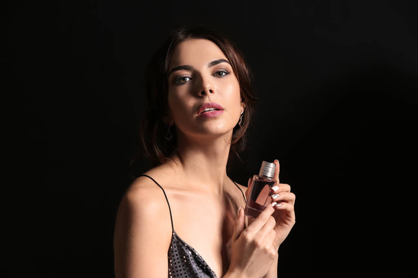 Beautiful young woman with bottle of perfume on dark background - Photo, Image