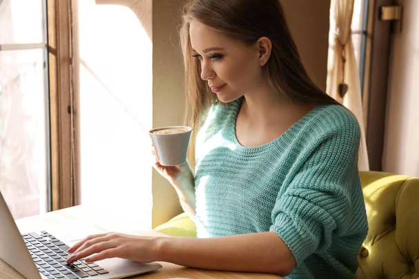 カフェでコーヒーを飲みながらノート パソコンを持つ若い女性 - 写真・画像