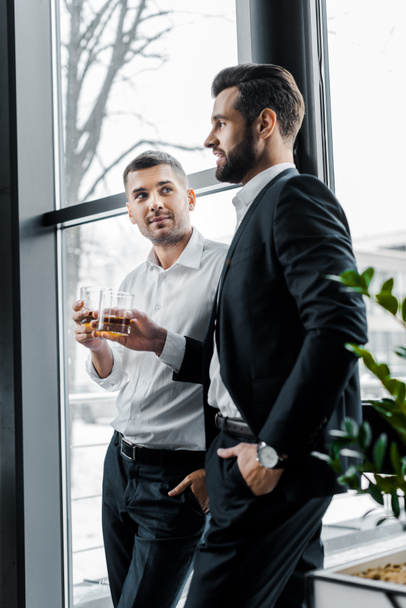 businessmen standing with hands in pockets and holding glasses with alcohol drinks  - Foto, afbeelding