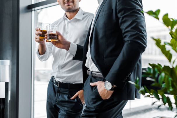 cropped view of businessmen standing with hands in pockets and holding glasses with alcohol drinks  - Photo, image