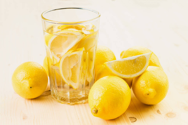 Glass of water with piece of lemon or glass of fresh hand made lemonade with lemons on wooden background. Copy space for text. - Foto, imagen