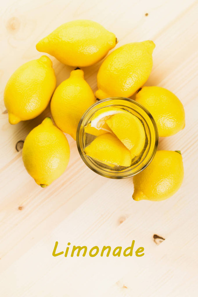 Verre d'eau avec un morceau de citron ou verre de limonade fraîche faite à la main avec des citrons sur fond en bois. Texte Lemonade. Vue d'en haut. Pose plate
. - Photo, image