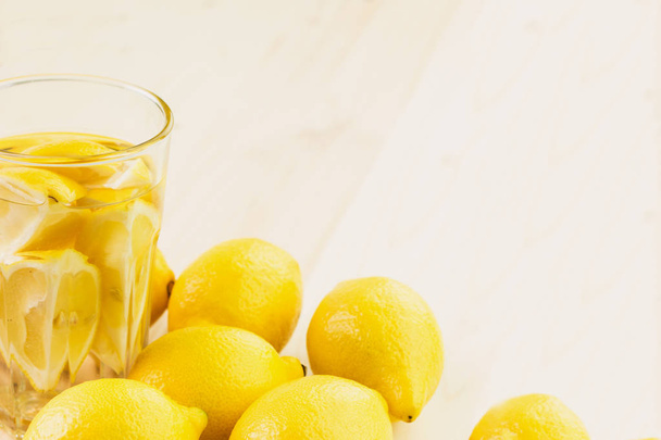 Glass of water with piece of lemon or glass of fresh hand made lemonade with lemons on wooden background. Copy space for text. - Photo, Image