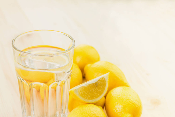 Verre d'eau avec un morceau de citron ou verre de limonade fraîche faite à la main avec des citrons sur fond en bois. Espace de copie pour le texte
. - Photo, image