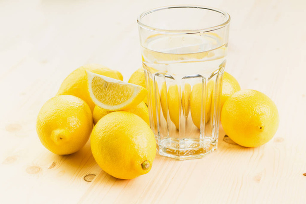 Glas Wasser mit Zitronenstück oder Glas frischer, handgemachter Limonade mit Zitronen auf Holzgrund. Kopierraum für Text. - Foto, Bild