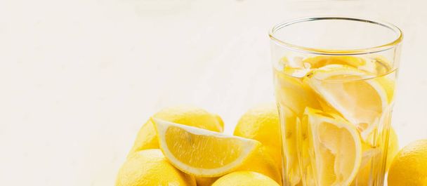 Glass of water with piece of lemon or glass of fresh hand made lemonade with lemons on wooden background. Copy space for text. - Photo, Image