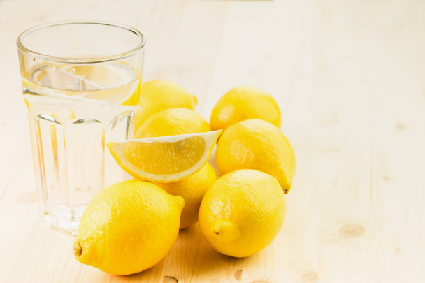 レモンの切れ端や新鮮な手のガラスと水のガラスは、木製の背景にレモンでレモネードを作った。コピーのテキストのための領域. - 写真・画像