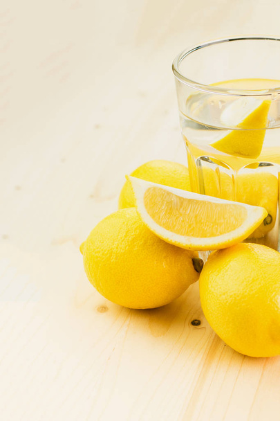 Glas water met een stukje citroen of een glaasje verse hand gemaakt limonade met citroenen op houten achtergrond. Ruimte voor tekst kopiëren. - Foto, afbeelding