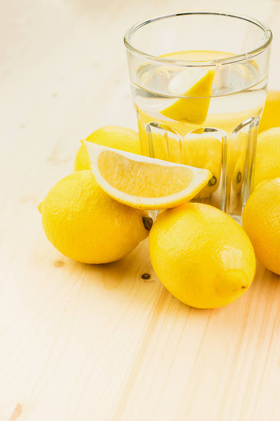 Bicchiere d'acqua con un pezzo di limone o un bicchiere di limonata fresca fatta a mano con limoni su sfondo di legno. Copia spazio per testo
. - Foto, immagini