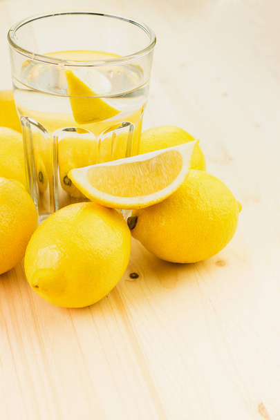 Glas water met een stukje citroen of een glaasje verse hand gemaakt limonade met citroenen op houten achtergrond. Ruimte voor tekst kopiëren. - Foto, afbeelding
