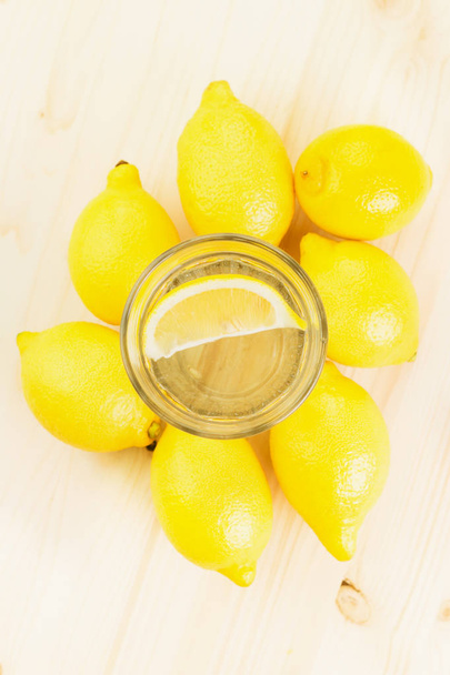Glas Wasser mit Zitronenstück oder Glas frischer, handgemachter Limonade mit Zitronen auf Holzgrund. Kopierraum für Text. Blick von oben. flache Lage. - Foto, Bild