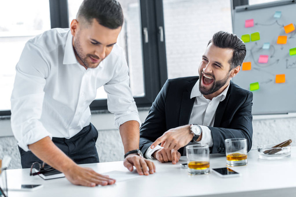 bearded businessman laughing near coworker in modern office  - Fotoğraf, Görsel