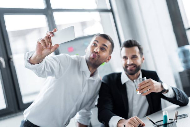 enfoque selectivo de hombres de negocios alegres tomando selfie en la oficina moderna
  - Foto, imagen