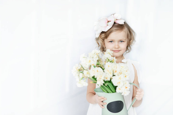girl holding narcissus in hands. Adorable smiling little girl holding flowers for her mom on mother's day. copy space - Zdjęcie, obraz