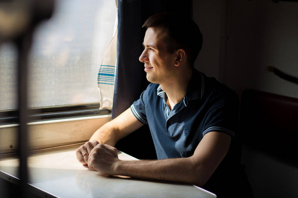 Молодой человек наслаждается поездкой на поезде - оставив машину дома, смотрит в окно, успевает полюбоваться пейзажем
 - Фото, изображение