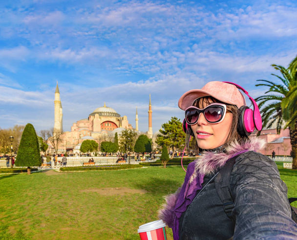 Piękna kobieta w kapeluszu z kawa na wynos, Okulary przeciwsłoneczne, słuchawki bierze selfie z widokiem na Kościół Hagia Sophia na tle hotelu sultanahmet, Stambuł, Shaki - Zdjęcie, obraz