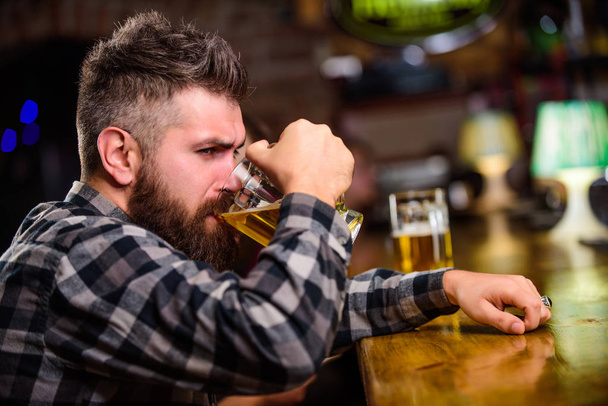 Order alcohol drink. Bar is relaxing place have drink and relax. Hipster relaxing at bar with beer. Man with beard spend leisure in dark bar. Brutal hipster bearded man sit at bar counter drink beer - Photo, image