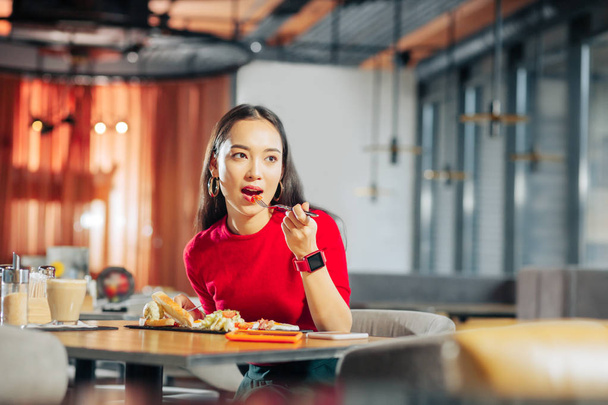 Dark-haired woman wearing red smart watch eating delicious lunch - Foto, imagen
