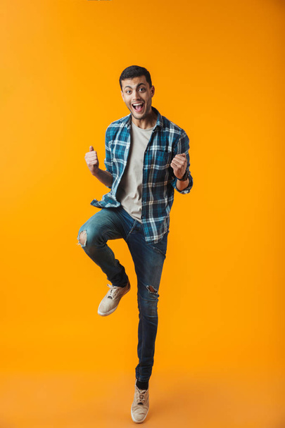 Full length portrait of a happy young man wearing plaid shirt isolated over orange background, jumping celebrating success - Foto, immagini