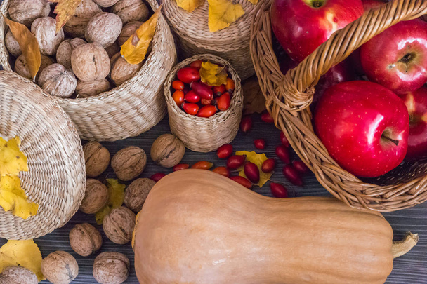 Walnuts, red apples in basket, rose hips, pumpkin and yellow leaves on a wooden surface, healthy food from nature. Concept of autumn background - Photo, Image