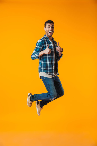 Full length portrait of a happy young man wearing plaid shirt isolated over orange background, jumping celebrating success - Foto, Imagem