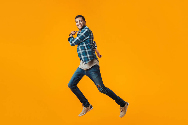 Full length portrait of a happy young man wearing plaid shirt isolated over orange background, jumping - Fotografie, Obrázek