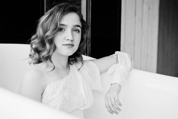 Pretty young curly gilrl in white dress sitting at bath. - 写真・画像