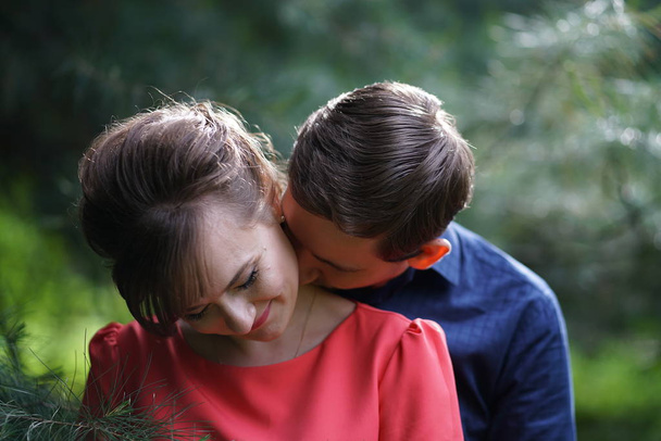 hübsches kaukasisches Liebespaar, das im grünen Sommerpark spaziert, lächelt, küsst und umarmt - Foto, Bild