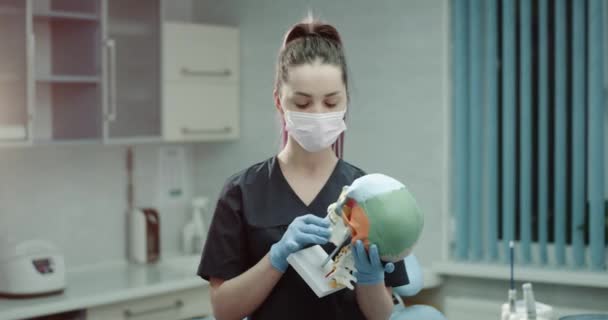 Young nurses assistant in front of the camera in a modern clinic room holding a big medical human skull. - Záběry, video