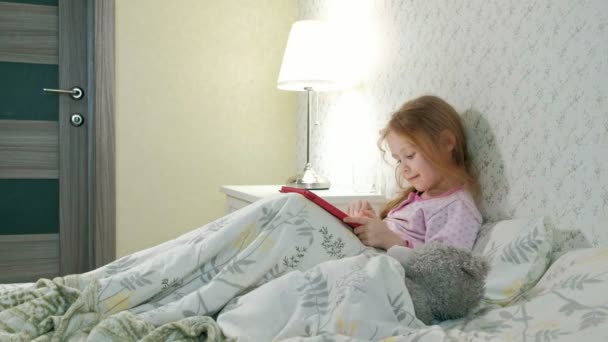 mała dziewczynka w łóżku gry na tablet - Materiał filmowy, wideo