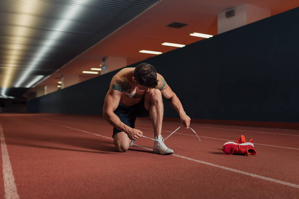Very fit man on a an indoor track preparing to run - Foto, imagen