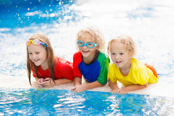Çocuklar yüzme havuzunda oynar. Çocuklar aile yaz tatili tropikal resort açık yüzme havuzunda yüzmeyi öğrenmek. Su ve splash eğlenmek için tatil genç çocuk. Çocuk ve bebek için güneş koruma. - Fotoğraf, Görsel