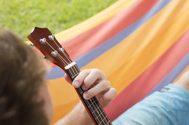 Деталь человека расслабляется на гамаке и играет на укулеле
. - Фото, изображение