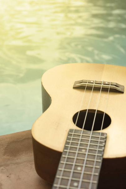Detail van ukulele met zwembad op de achtergrond. - Foto, afbeelding