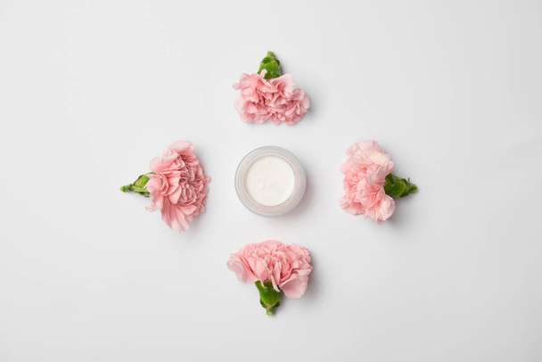 Plat leggen van anjers bloemen in rhombus schikken en crème container op witte achtergrond - Foto, afbeelding