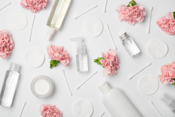 Vista dall'alto di diverse bottiglie cosmetiche, fiori di garofano, bastoncini di cotone e pastiglie cosmetiche su sfondo bianco
 - Foto, immagini