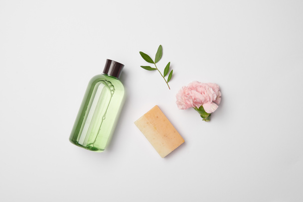Top view of different cosmetic bottles, soap, tea plant branch and carnation flower on white background - Photo, Image