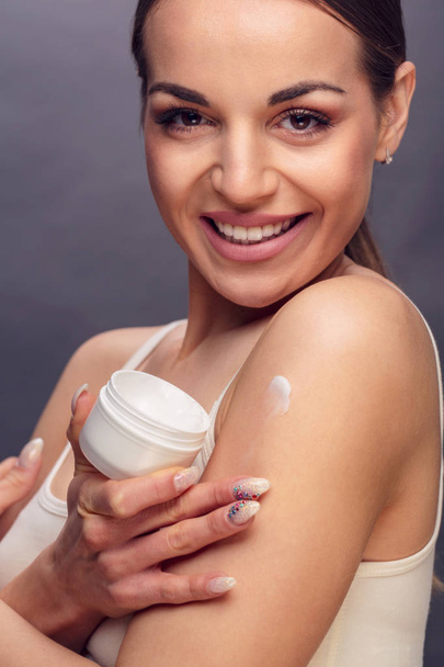 Молода усміхнена жінка застосовує концепцію догляду за шкірою зволожувач
 - Фото, зображення